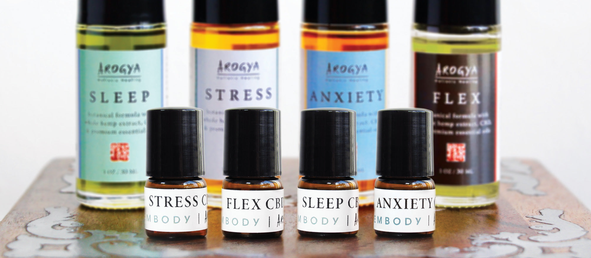 Close up of four 1mL starter size CBD oils with the same four oils in larger 1 oz. bottles blurred in the background.