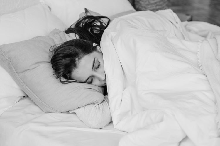 Woman sleeping on her side in bed with a blanked pulled up to her face.